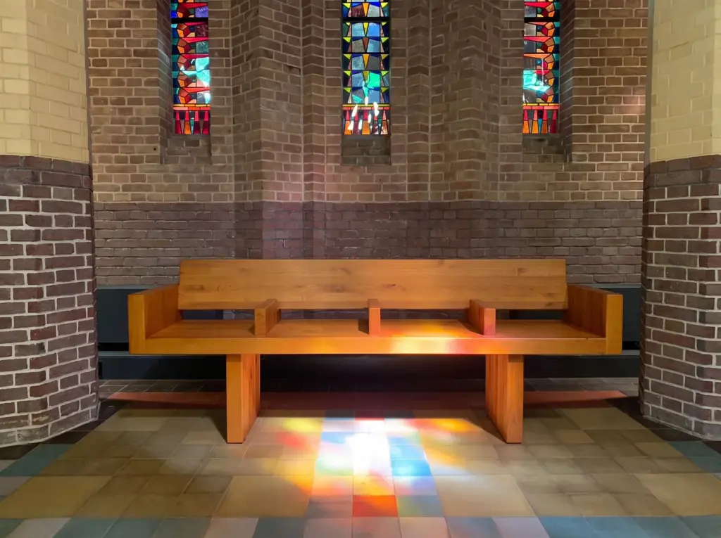 Een eikenhouten bank in de kapel van Adelbert, met gekleurd licht van de glas-in-loodramen op de vloer