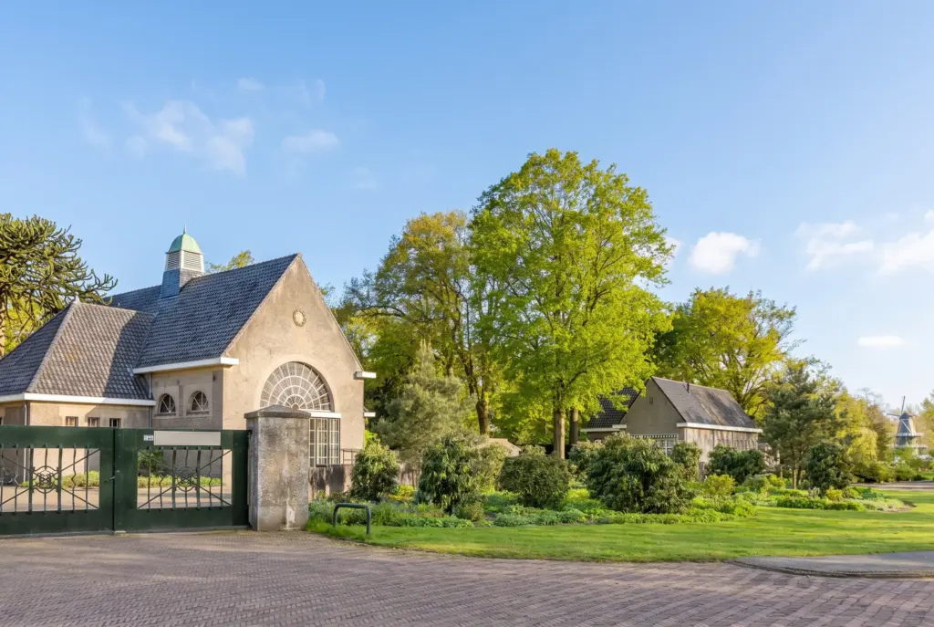 Het aulagebouw van de Algemene Begraafplaats Herfstlaan in Heemstede met een groot waaiervormig raam, een groen torentje en het groene toegangshek