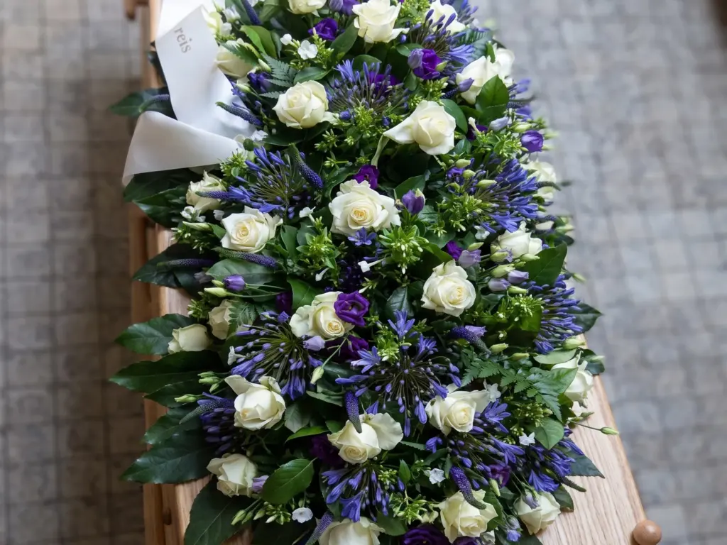 Een bloemstuk van witte rozen, blauwe agapanthus en paarse lisianthus op een lichte kist