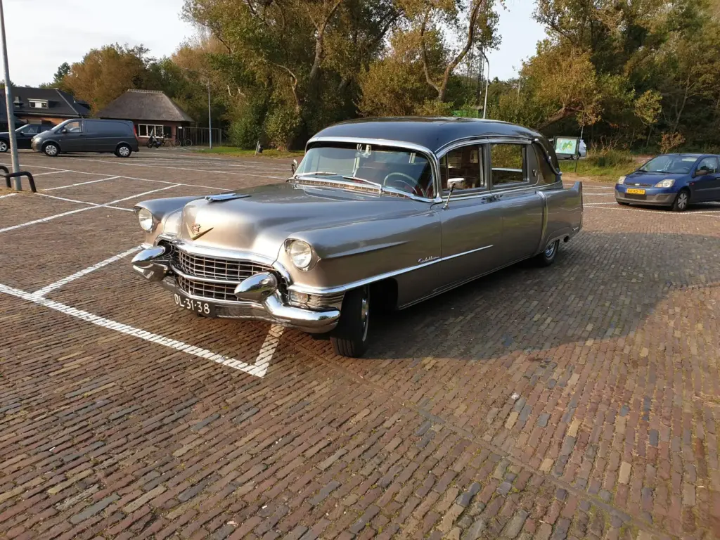 De zilvergrijze Cadillac rouwauto uit 1955 van Uitvaartverzorging Uitendaal op een parkeerterrein