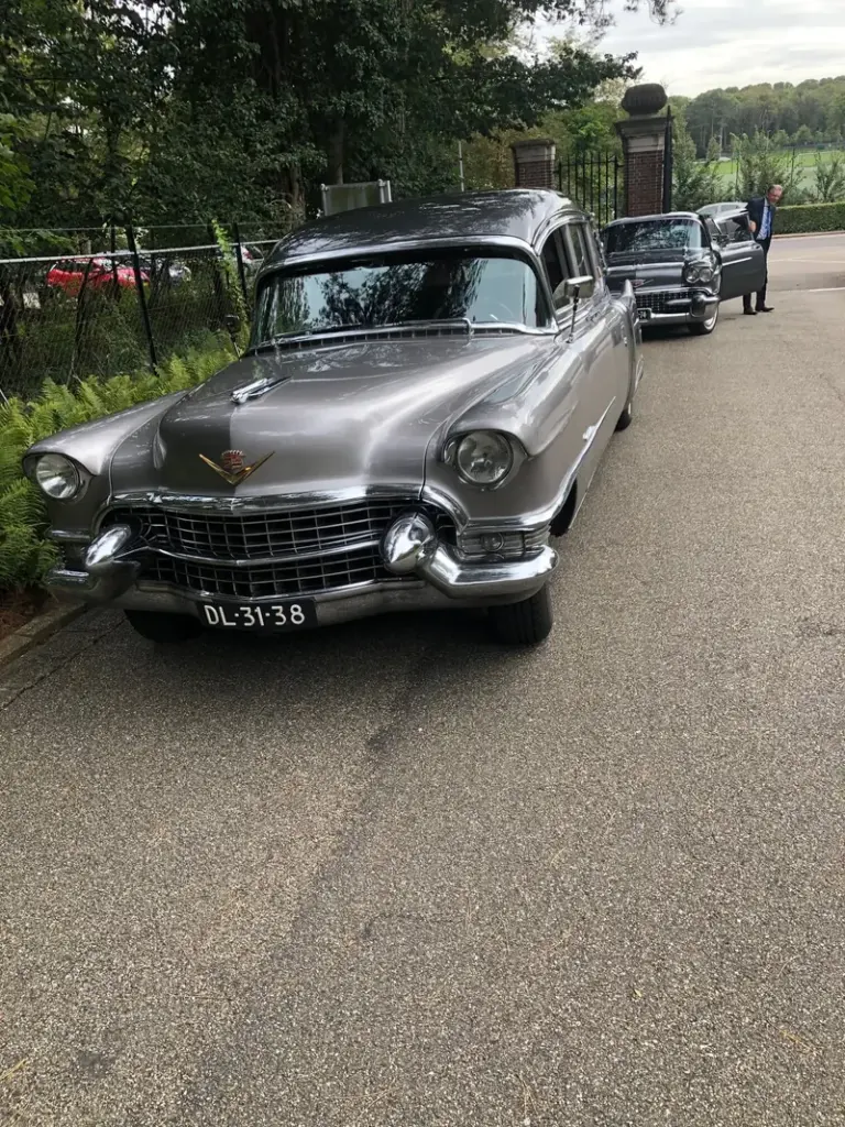 De klassieke Cadillac rouwauto van Uitendaal op straat, met de volgauto erachter