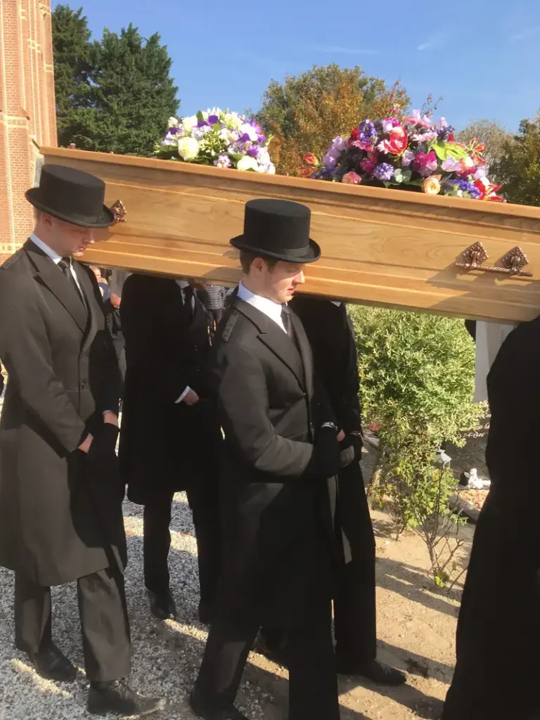 Dragers in zwart met hoge hoed dragen een eikenhouten kist met bloemen