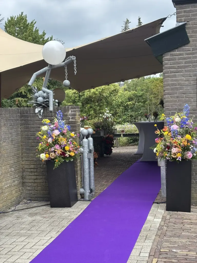 Een paarse loper tussen twee grote boeketten bij de ingang naar een afscheid