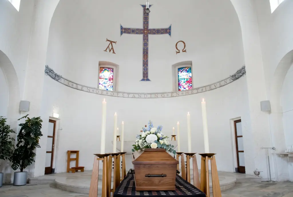 De kapel van begraafplaats Sint Jozef in Haarlem met een mozaïekkruis, hoge kaarsen en een eikenhouten kist met bloemen