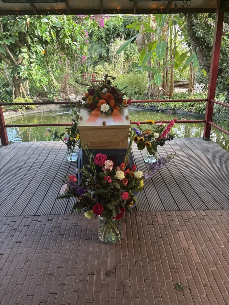 Een lichte kist met bloemen op een houten vlonder aan het water in een tuin