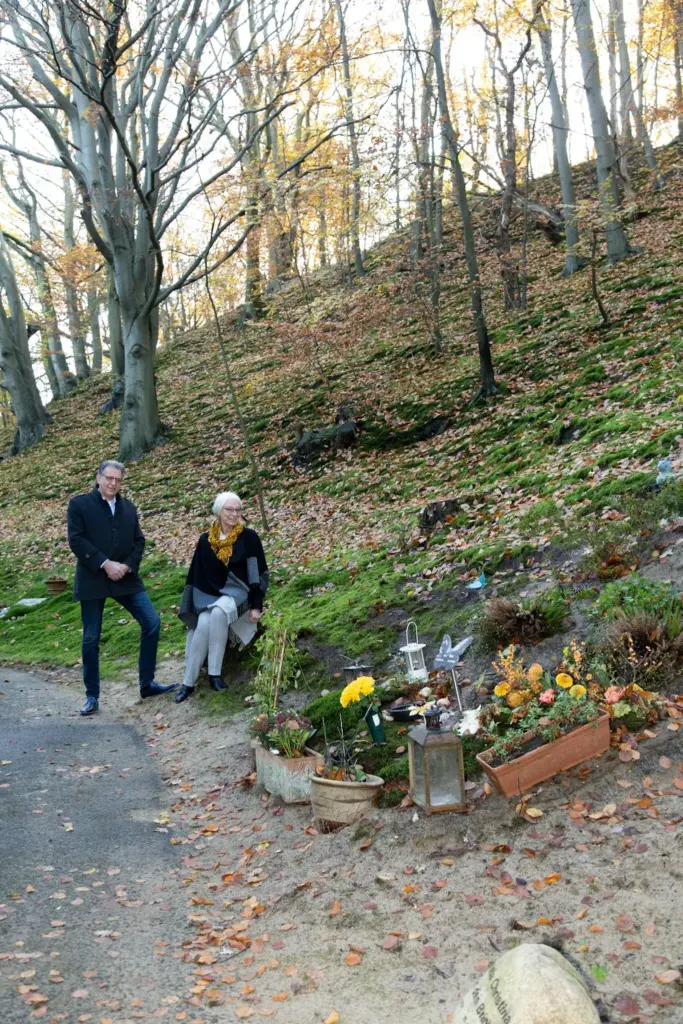 Martin Uitendaal en Sonja Raijmakers bij een met bloemen en lantaarns beplante helling op een begraafplaats