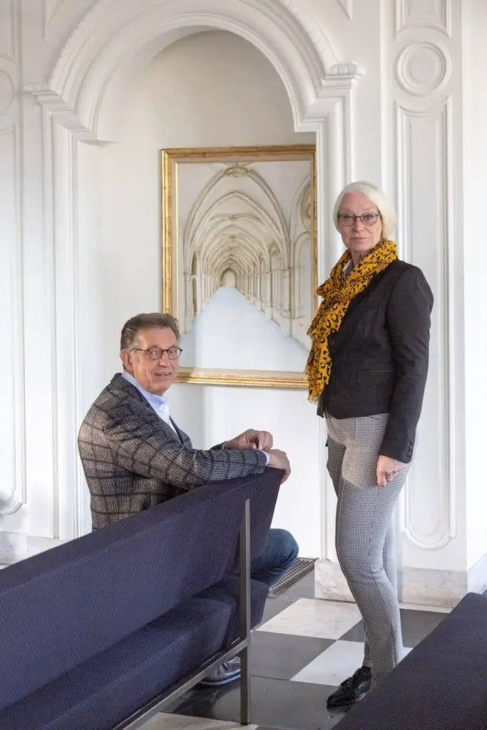 Martin Uitendaal zit in een bank in een aula, Sonja Raijmakers staat naast hem