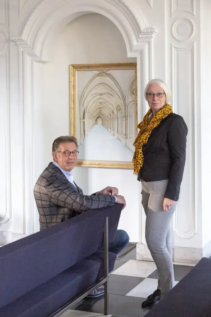 Martin Uitendaal zit in een bank in een aula, Sonja Raijmakers staat naast hem