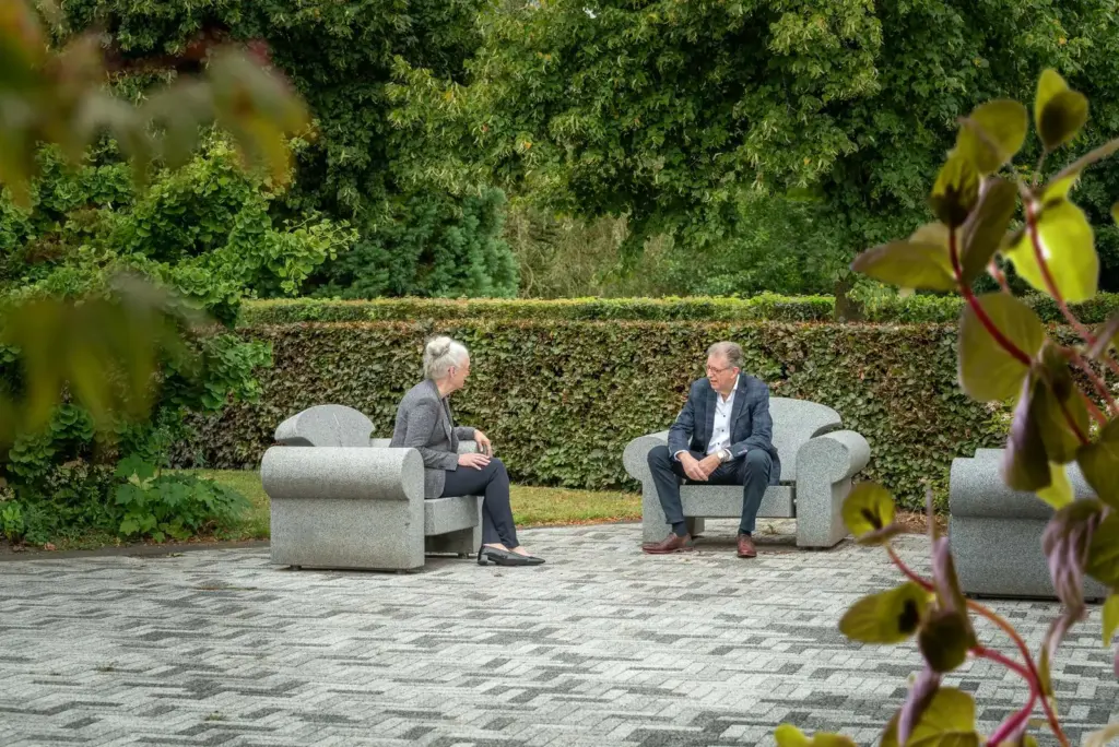 Martin Uitendaal en Sonja Raijmakers in gesprek, elk in een granieten stoel in een tuin