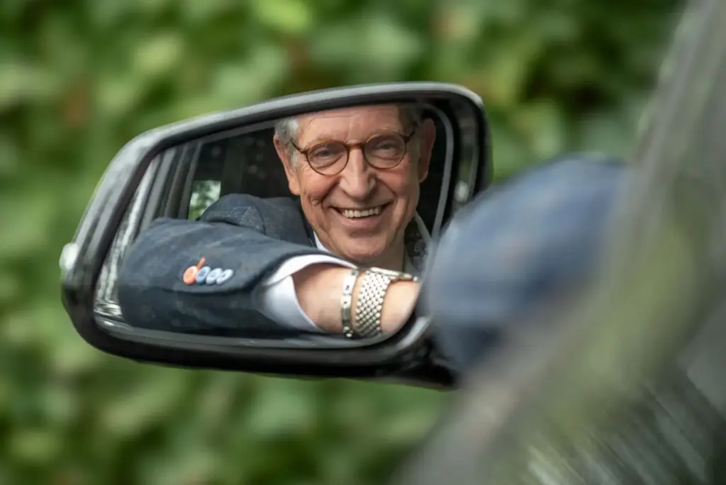 Martin Uitendaal lachend in de zijspiegel van een auto