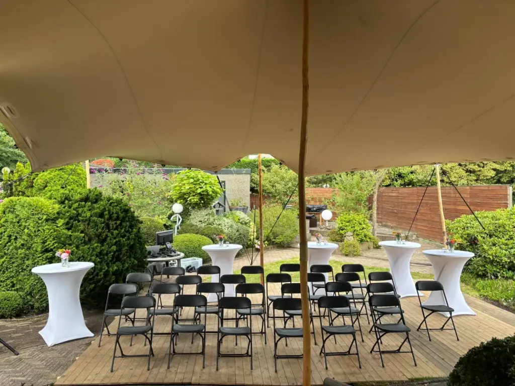Rijen stoelen onder een tent in een tuin, klaar voor een plechtigheid
