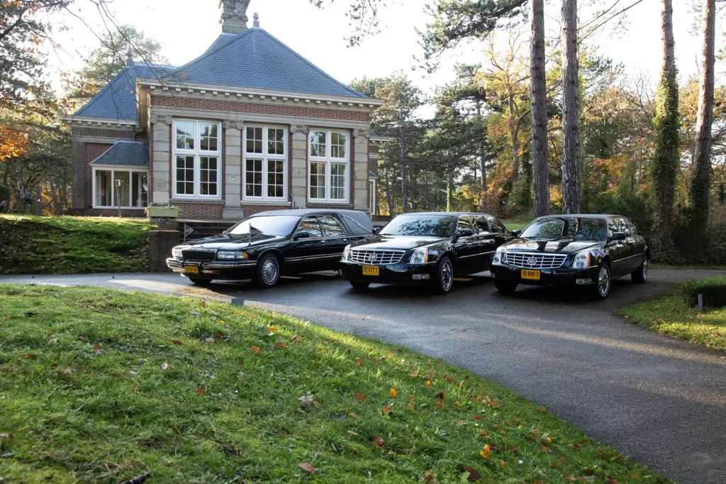 Drie zwarte rouwauto's van Uitendaal op de oprit van een aula in het najaar