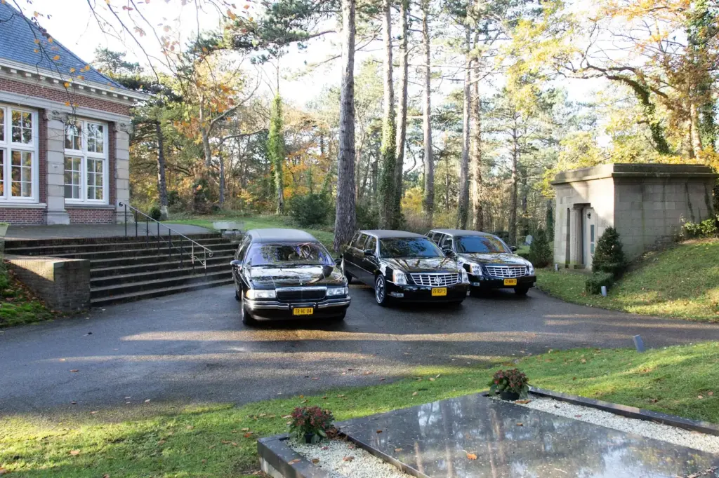 Zwarte rouwauto's van Uitendaal voor een aula in het bos