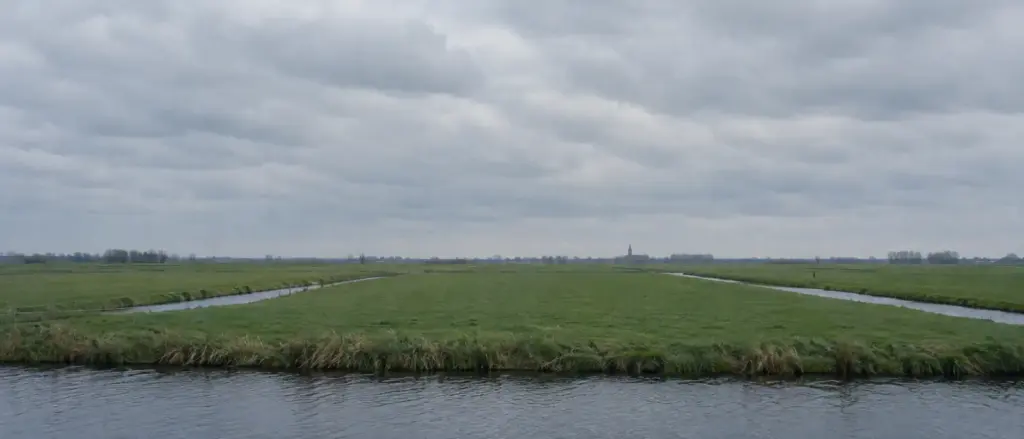 Vlak polderland met rechte sloten en een heel klein kerktorentje aan de horizon