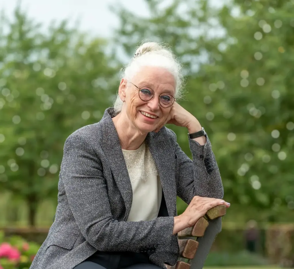 Sonja Raijmakers zit lachend op een bankje, met haar hand onder haar kin