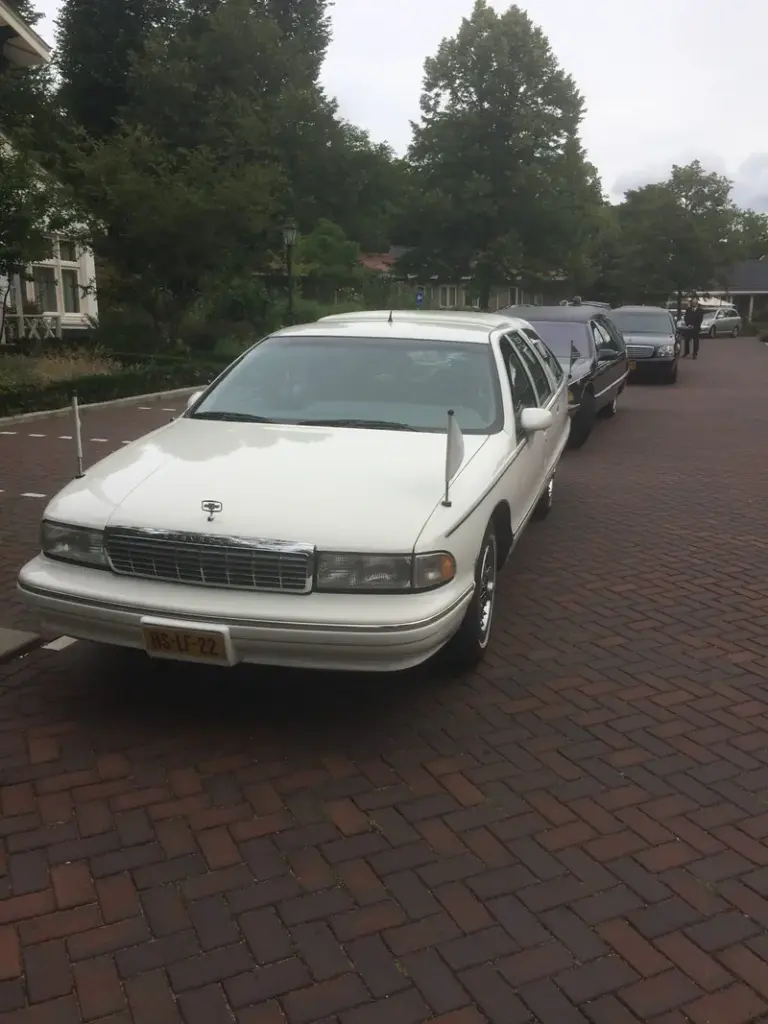 De witte rouwauto van Uitendaal staat klaar op een oprit